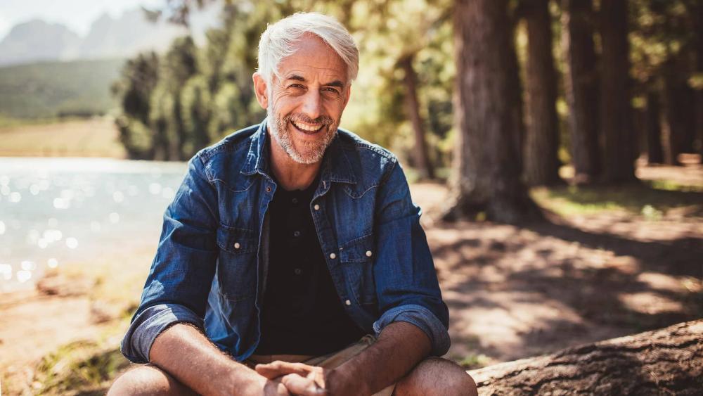 man smiling sitting on log infront of lake