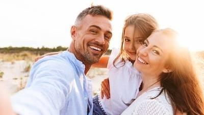 mom, dad, and daughter smiling on the beach